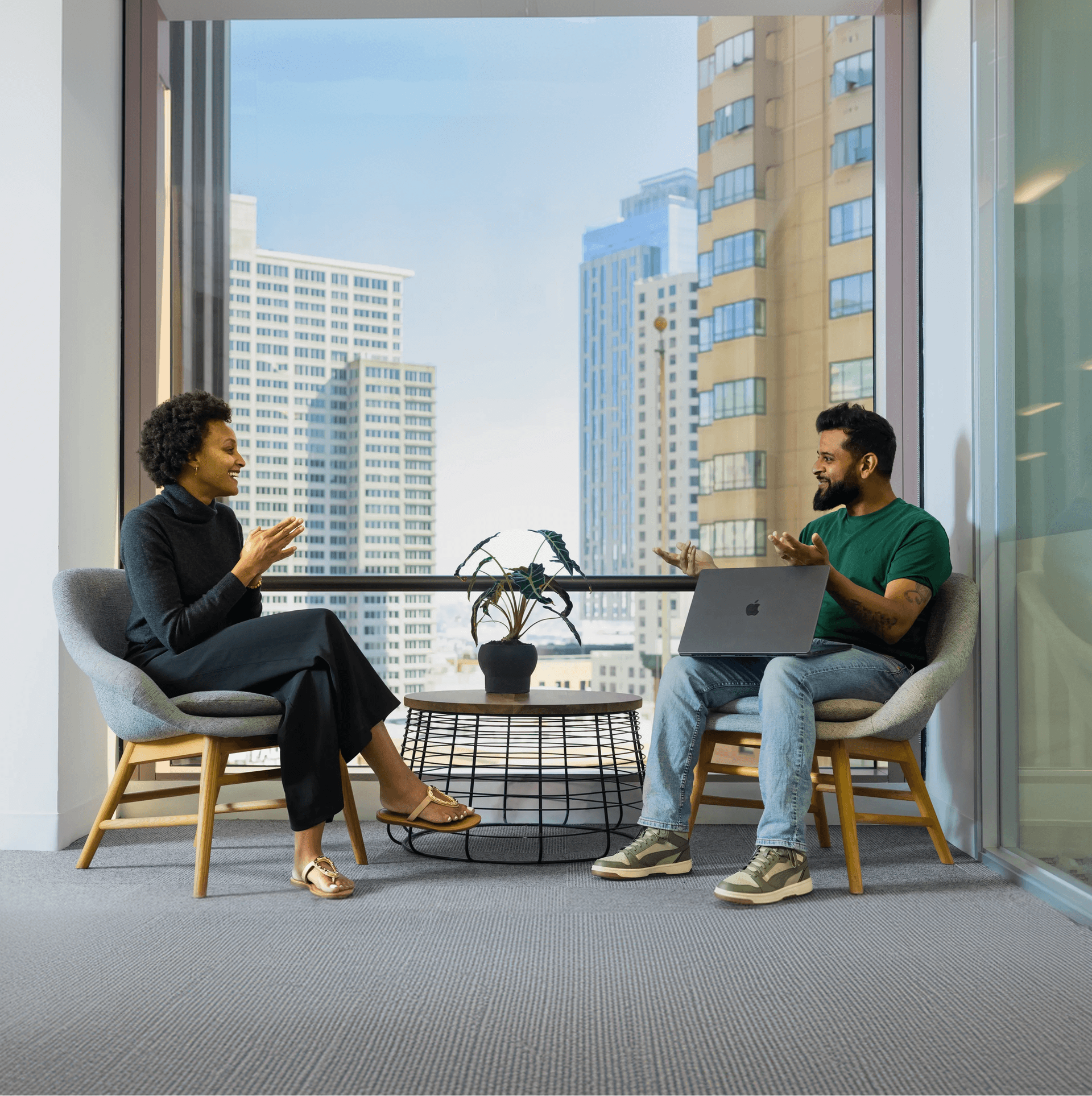 A man and a woman in professional attire having a collaborative discussion in a modern office with a city skyline view.